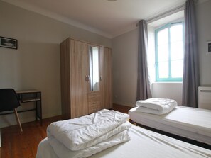 Ein Schlafzimmer mit zwei Betten, einem Holzschrank, einem Schreibtisch und einem Fenster mit Vorhängen.