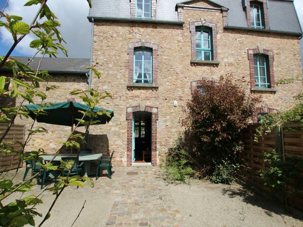 Ein Steinhaus mit einer Ziegelhaustür, einer kleinen Terrasse mit Tisch und Stühlen und einem grünen Sonnenschirm.