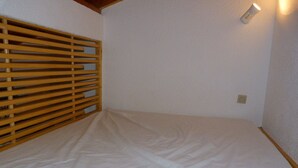 Une pièce avec une cloison en lattes de bois, un matelas blanc et un luminaire fixé au mur.