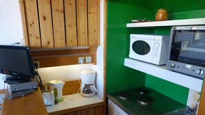 Une cuisine de taille réduite, dotée de meubles en bois, d’un four à micro-ondes, d’une cuisinière et d’une machine à café.