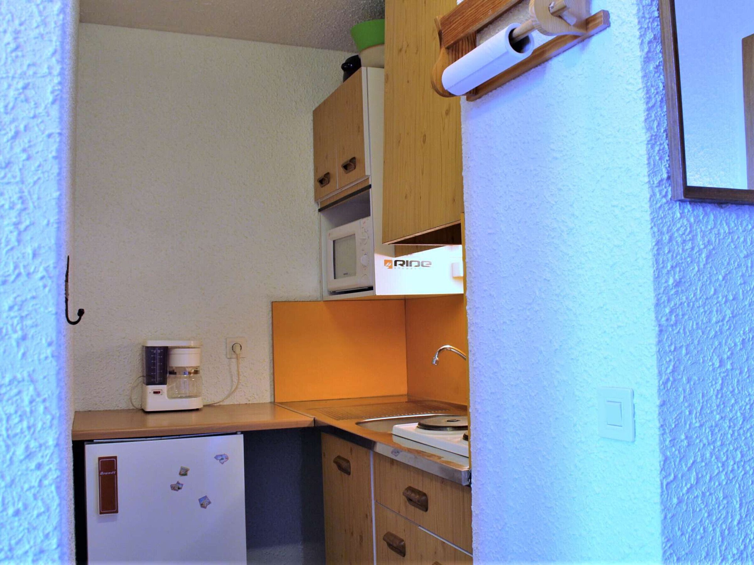 Eine kleine Küchenzeile mit Kühlschrank, Mikrowelle, Kaffeemaschine und Spüle.