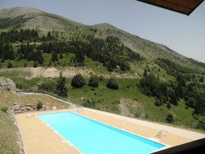Relax by the serene pool surrounded by lush green hills and a clear sky.