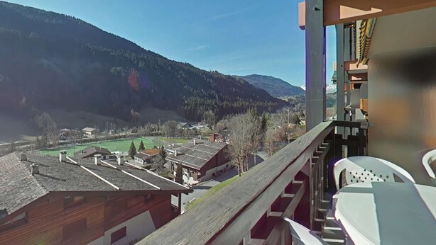 A balcony with a view of a village, mountains, and a sports field. - Comfortable studio with parking in Grand Bornand (Le Grand-Bornand)