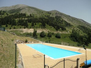 Relax by the serene pool surrounded by lush green hills and a clear sky.