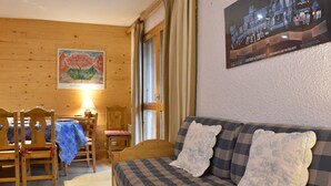 Ein gemütliches Zimmer mit Holzboden, einer Couch mit gemusterten Kissen, einem Esstisch mit Stühlen und einem Bild an der Wand.