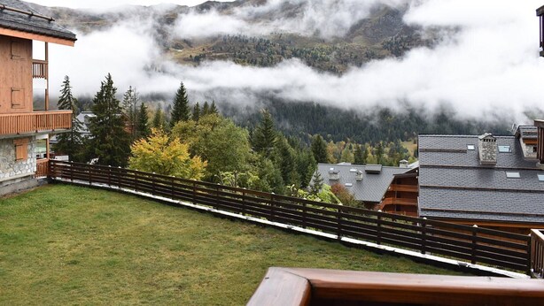 Eine Berglodge mit einer Holzdar Terrasse und Blick auf ein bewaldetes Tal.