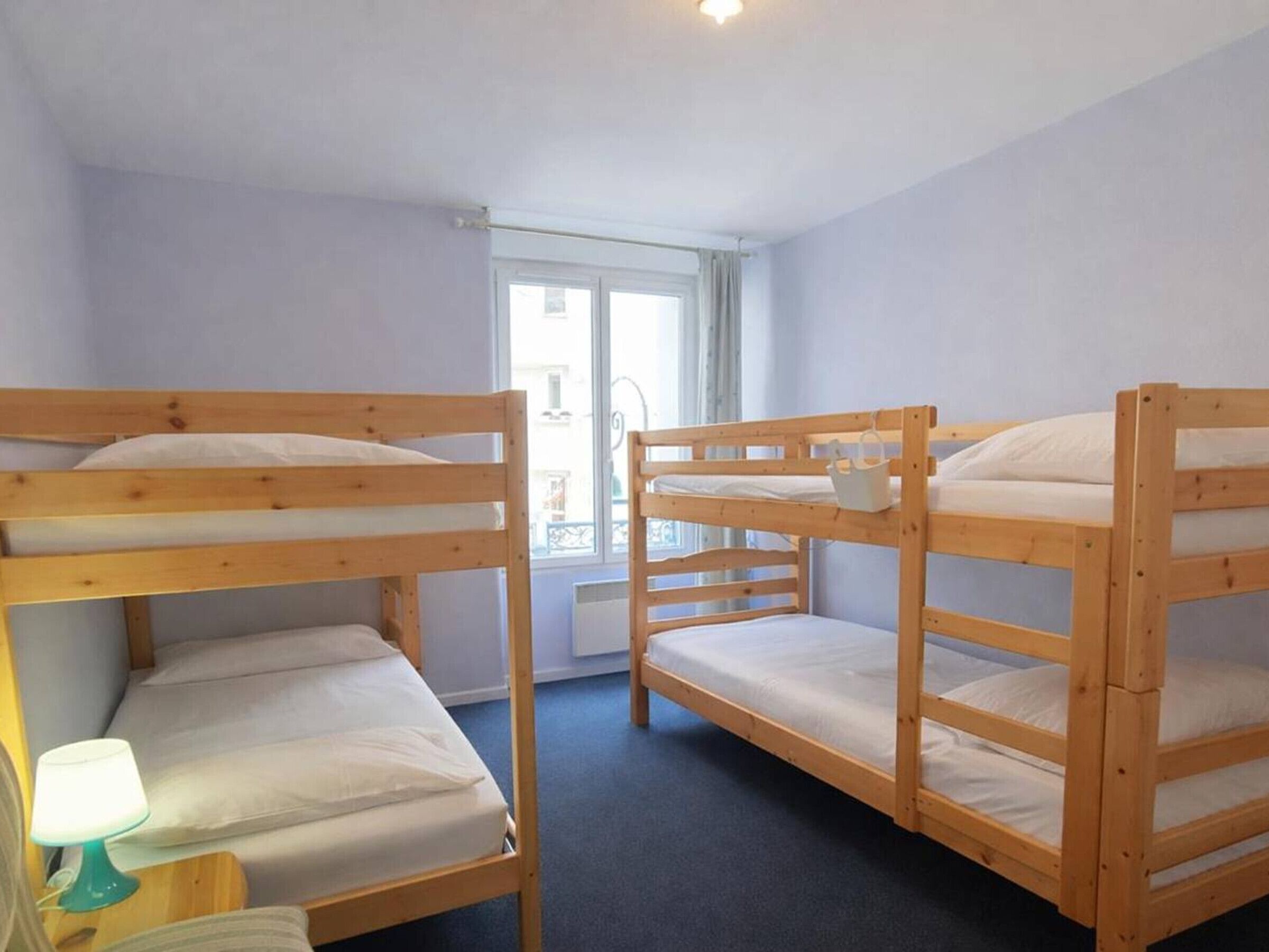 Una habitación con tres literas, una ventana con cortinas, una lámpara en una mesita de noche y un radiador.