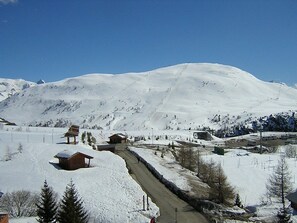A snow-covered mountain with a clear sky. There are wooden buildings and a road leading up the mountain.