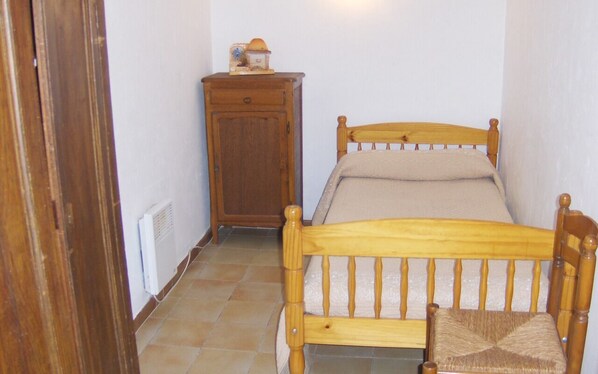 A small, narrow room with a wooden bed, a wooden nightstand, and a radiator.