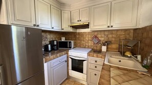 Una cocina con gabinetes blancos, un refrigerador de acero inoxidable, un microondas, una estufa y un lavamanos.