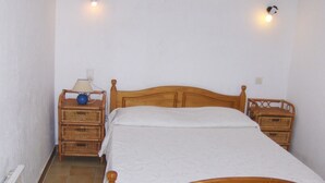 Une petite chambre avec un lit simple, une tête de lit en bois, une table de chevet avec une lampe et une table de nuit en osier.
