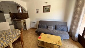 Ein kompakter Wohnraum mit Küchenzeile, einer Couch, einem Esstisch und einem kleinen Fenster.