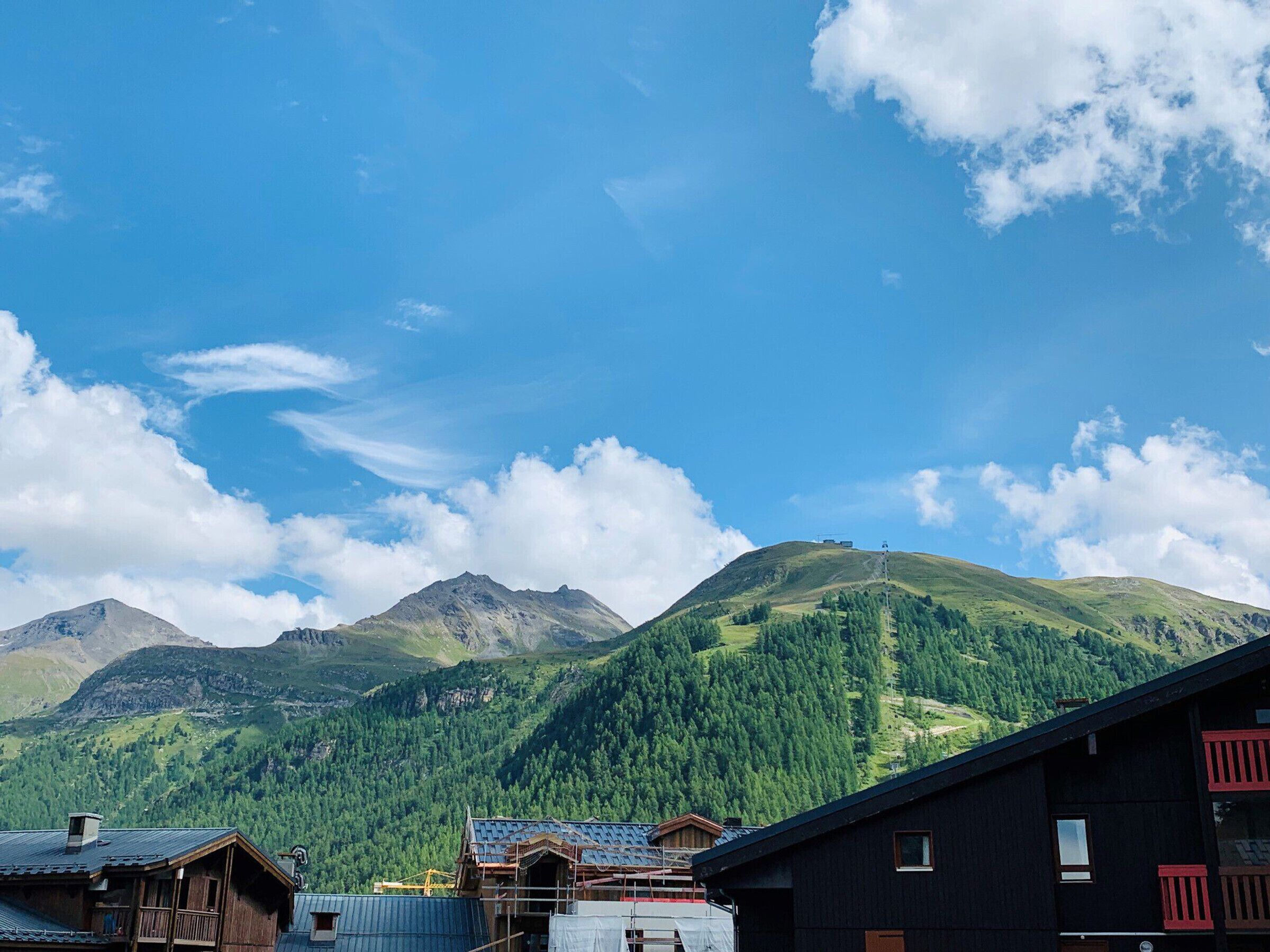 A mountain village with traditional wooden buildings, a clear blue sky, and lush green hills in the background.