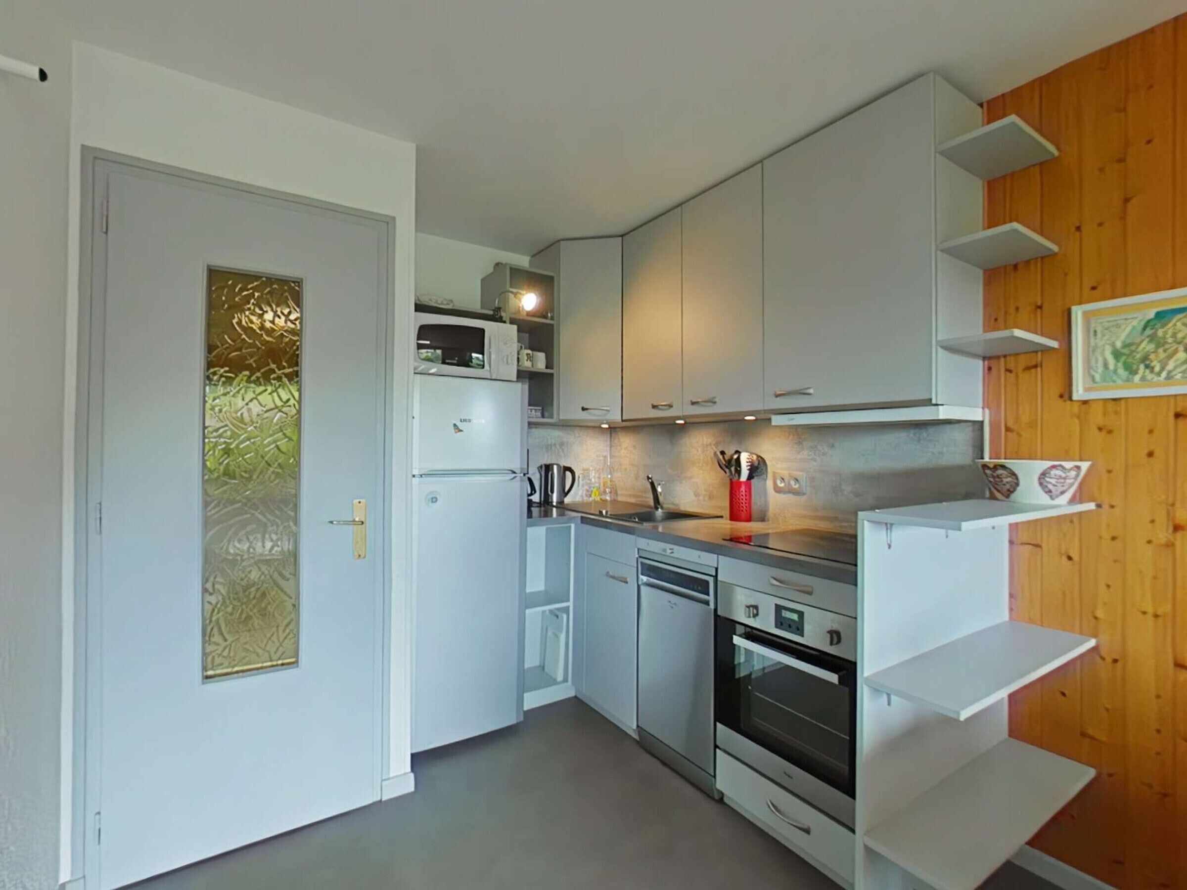 Een kleine keuken met witte kastjes, een magnetron, een koffiezetapparaat en een klein oven.