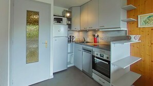 Una cocina compacta con armarios blancos, un microondas, una cafetera y un horno pequeño.