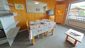 Un comedor con una mesa preparada para cuatro personas, un televisor, armarios de madera y una ventana con vistas a edificios.