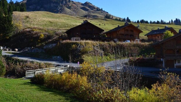 Un pueblo rural de montaña con casas de madera tradicionales, cielo despejado y una colina destacada al fondo.
