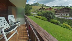 Un balcón con sillas blancas, piso de madera y vistas a colinas verdes y casas de madera tradicionales.