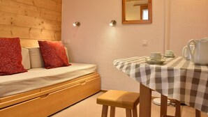 A cozy room with a wooden bed, a small table with a checkered tablecloth, and a mirror on the wall. - Cozy Studio, Ski-In/Ski-Out, Near Shops & Restaurants, Méribel Centre (Méribel)