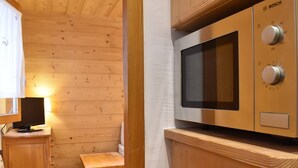 A compact kitchen with a Bosch microwave, wooden cabinets, a small wooden table, and a window with a curtain. - Cozy Studio, Ski-In/Ski-Out, Near Shops & Restaurants, Méribel Centre (Méribel)