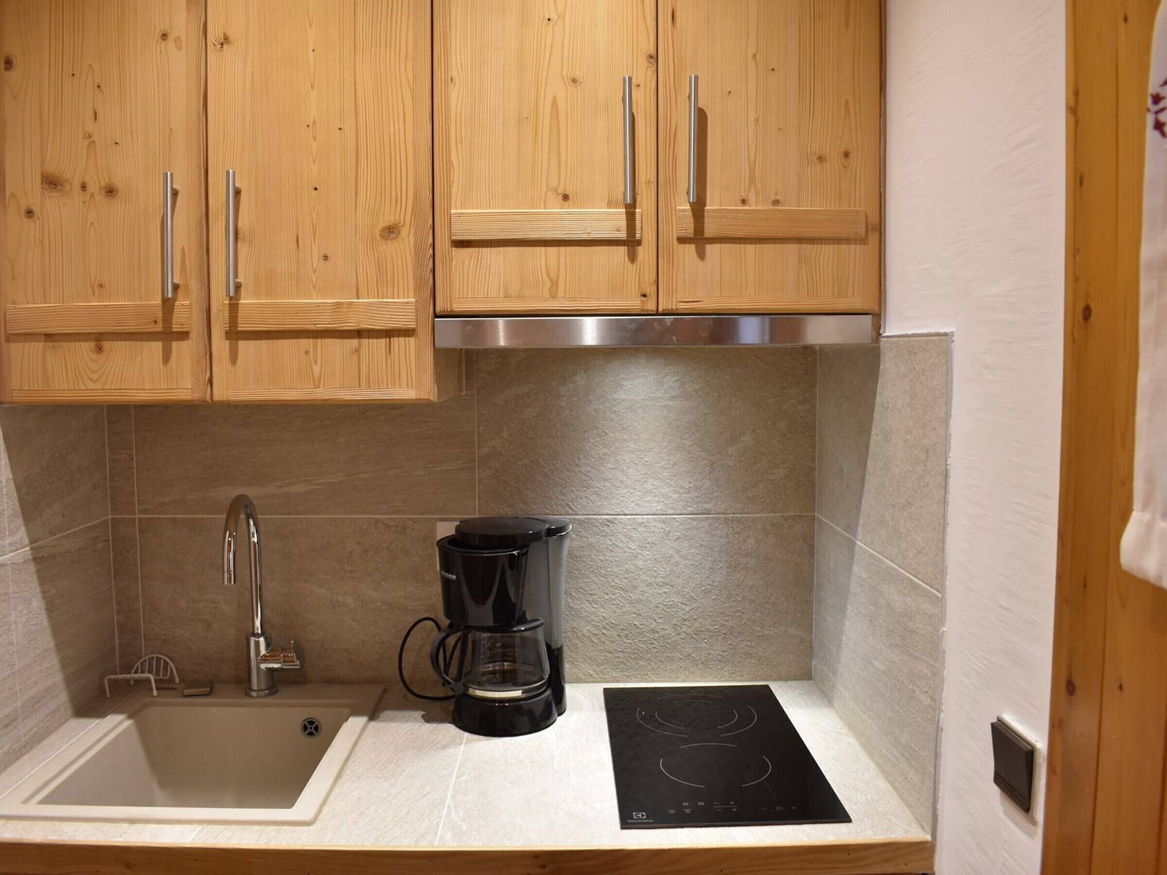 A kitchen with wooden cabinets, a stainless steel range hood, a sink, a coffee maker, and an induction cooktop.