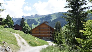 A wooden chalet with a balcony, surrounded by lush greenery and mountains in the background. - Cozy Studio, Ski-In/Ski-Out, Near Shops & Restaurants, Méribel Centre (Méribel)