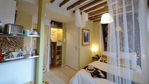 Une chambre d’hôtel compacte comprenant un coin cuisine, un lit à baldaquin et un petit coin salon.
