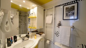 Une salle de bain moderne avec un lavabo blanc, un miroir et un porte-serviettes. On y trouve un espace douche avec une porte en verre et un porte-serviettes au-dessus. Une photo encadrée est accrochée au mur.