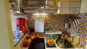 Une cuisine équipée d’une plaque de cuisson à induction noire, d’un évier et d’un assortiment de fruits et de légumes disposés sur le plan de travail.