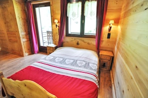 A wooden cabin bedroom with a bed, two bedside tables, and a window with curtains.