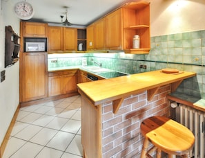 A kitchen with wooden cabinets, a microwave, a sink, and a brick island with stools.