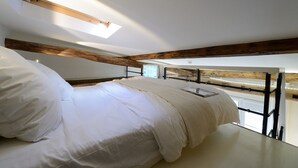 A bedroom with a sloped ceiling, exposed wooden beams, a bed with white bedding, and a skylight. - D4DD Family white (Paris)