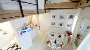 A compact hotel room with a checkered floor, a small dining area with a table set for two, and a wall adorned with framed photographs. - D4DD Family white (Paris)