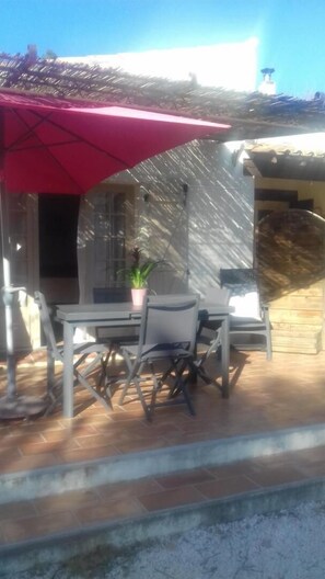An outdoor patio with a table and chairs, a red umbrella, and a potted plant.