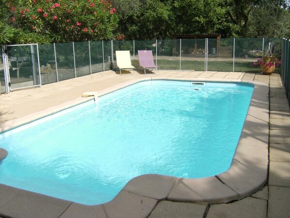 A rectangular swimming pool with a tiled deck, surrounded by a metal fence and two lounge chairs.
