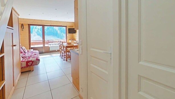 A bedroom with a bed, a wooden wardrobe, and a window with a view of trees.