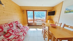 A cozy wooden cabin with a sofa, dining table, chairs, and a TV.