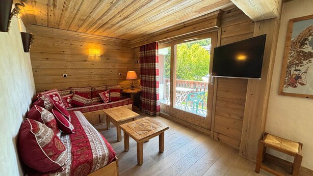 Een gezellig houten hutje van binnen met een bank, een kleine tafel en een aan de muur bevestigde televisie.