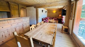 Een houten interieur met een lange eettafel, stoelen en een gezellige zithoek met kussens.