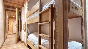 Een slaapkamer met stapelbedden, houten wanden en vloeren, een deur die naar een andere kamer leidt, en een gang.