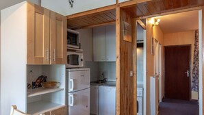 A compact kitchen with wooden cabinets, a microwave, a refrigerator, and a dishwasher.
