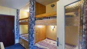 A compact room with bunk beds, a door, a small table, and a wall-mounted light fixture.