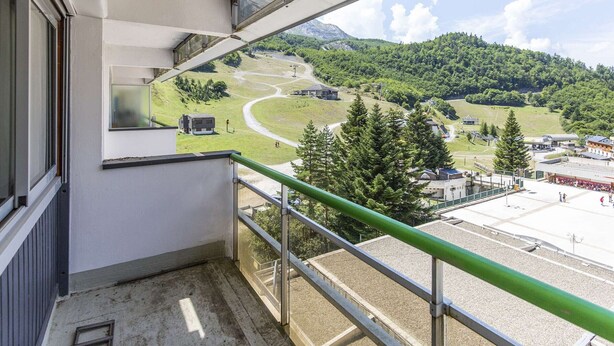 A balcony with a view of a mountainous landscape, a gravel area, and a building with a green roof.