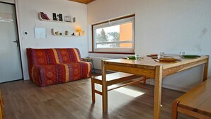 Un salon chaleureux avec une table à manger en bois, un canapé coloré et une fenêtre donnant sur les arbres.