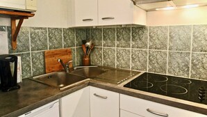 Une cuisine avec des meubles blancs, un évier en acier inoxydable, une plaque de cuisson noire et une planche à découper en bois.
