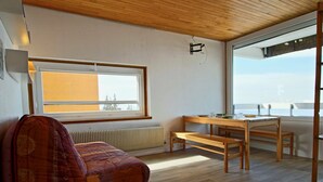Une pièce chaleureuse avec un plafond en bois, une grande fenêtre, un canapé, une table en bois avec des bancs, et une vue sur le ciel.