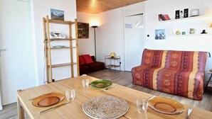 Un salon chaleureux avec une table en bois dressée pour le repas, un canapé et une échelle appuyée contre le mur.