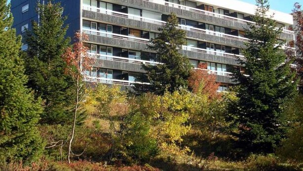 Un immeuble à plusieurs étages doté de balcons, entouré d’arbres et de végétation.