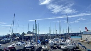 A marina with multiple sailboats docked, a covered area, and a large crane structure in the background.