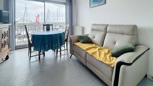 A living room with a sofa, a table, and a view of a cityscape through large windows.